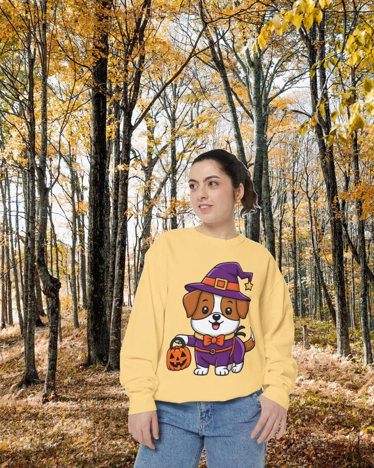 Woman wearing yellow Halloween sweatshirt featuring cartoon dog in witch costume holding pumpkin, autumn forest background