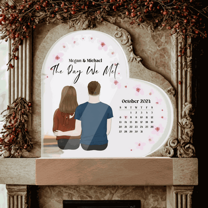 Personalized acrylic heart plaque with couple illustration, calendar, and "The Day We Met" inscription, ideal keepsake gift for anniversaries or weddings.